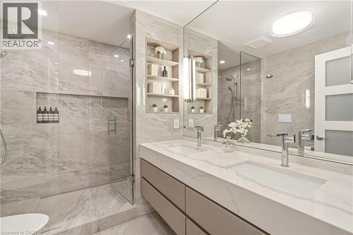Dual integrated sinks with chrome faucets, a frameless glass shower enclosure, built-in shower niche, recessed shelving, and a large wall-mounted mirror - 5056 New Street Unit# 4, Burlington, ON 
