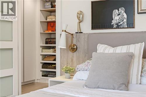 Custom built-in closet with integrated shelving, wood-finish flooring, wall-mounted sconce, and upholstered headboard - 5056 New Street Unit# 4, Burlington, ON 