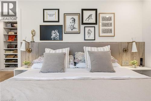 Built-in headboard featuring a fabric-padded panel and wood-finish side panels, integrated wall sconces, floating bedside tables, and a walk-in closet with built-in shelving - 5056 New Street Unit# 4, Burlington, ON 