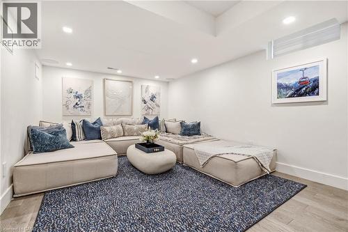 Sophisticated recreation room showcasing a sectional seating arrangement with coordinating throw pillows, recessed ceiling lighting, wood-finish flooring, a geometric patterned area rug, and framed ar - 5056 New Street Unit# 4, Burlington, ON 