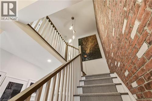 Staircase featuring wood railings, exposed brick wall, recessed lighting, and a modern light fixture - 5056 New Street Unit# 4, Burlington, ON 