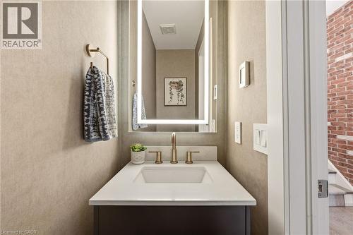 Vanity with an integrated rectangular sink, brass-finish faucet, and a lighted mirror - 5056 New Street Unit# 4, Burlington, ON 