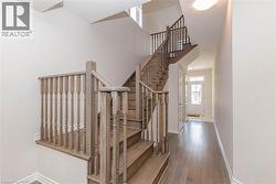 Two-story wooden staircase with decorative balusters, wood-finish flooring, and a white paneled entry door - 