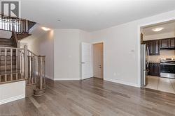 Hardwood-finish flooring, staircase with wood banister, white trim, recessed lighting, and kitchen with stainless steel appliances - 