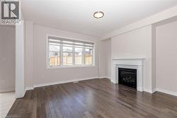 Rich wood-finish flooring, a contemporary fireplace with white mantel, a large window, and a modern ceiling fixture - 