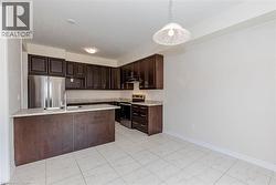 Kitchen featuring dark wood cabinetry, a large island with an undermount sink, stainless steel appliances, and tile flooring - 