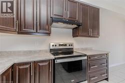Dark wood-finish cabinetry, stainless steel range, built-in range hood, light-toned countertops, and tile flooring - 
