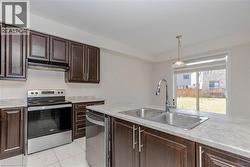 Kitchen featuring dark wood-finish cabinetry, stainless steel appliances, a dual basin sink with a gooseneck faucet, and light-toned countertops - 