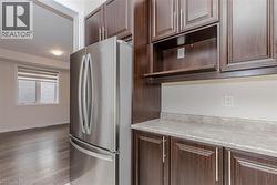 Stainless steel refrigerator, wood-finish flooring, dark wood cabinetry, light-toned countertops, and recessed lighting - 