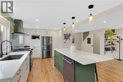 Gourmet kitchen featuring a large central island with seating, stainless steel appliances, white cabinetry with gold-toned hardware, wood-finish flooring, and a green tile backsplash - 311 Misty Crescent, Kitchener, ON - Indoor Photo Showing Kitchen With Stainless Steel Kitchen With Upgraded Kitchen