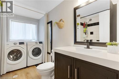 Integrated laundry area with side-by-side washer and dryer, wood-finish flooring, dark wood vanity with white countertop, and a framed mirror - 311 Misty Crescent, Kitchener, ON - Indoor Photo Showing Laundry Room