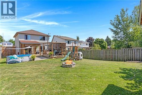 Spacious backyard featuring a large grass area, wood privacy fence, and a stone fire pit - 311 Misty Crescent, Kitchener, ON - Outdoor With Backyard