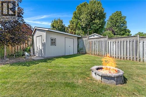 Manicured backyard featuring a stone fire pit, wood privacy fencing, a storage shed with two doors, and mature trees - 311 Misty Crescent, Kitchener, ON - Outdoor