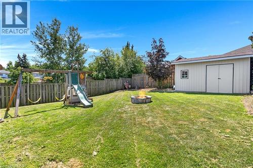 Expansive backyard featuring a manicured lawn, a built-in fire pit, privacy fencing, a storage shed with double doors and a window, and a play structure with a slide and swings - 311 Misty Crescent, Kitchener, ON - Outdoor With Backyard