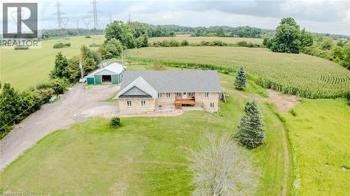 Stone exterior property with a shingled roof, featuring a wooden deck, mature evergreen trees, and an expansive lawn - 107 6Th Line Line, Haldimand, ON - Outdoor With View