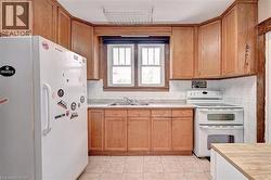 Kitchen featuring a double basin sink, white tile backsplash, wood-finish cabinetry, and neutral-toned floor tiling - 