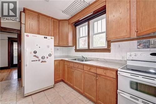 Kitchen featuring wood cabinetry, a double basin stainless steel sink, white tiled backsplash, and light-toned countertop surfaces - 147 Courtland Avenue E, Kitchener, ON - Indoor Photo Showing Kitchen With Double Sink