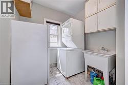 Laundry area featuring a utility sink, wall-mounted cabinetry, a window, and tile flooring - 