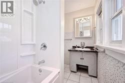 Bathroom featuring a white bathtub with an integrated shower, chrome fixtures, a single-pane window, a vanity with a dark countertop, and mosaic wall tiling - 