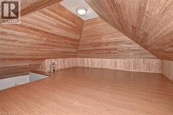 Expansive loft space featuring wood-finish flooring, sloped wood-paneled ceilings, and wood-paneled wainscoting - 