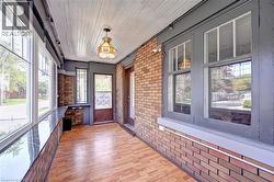 Enclosed porch featuring wood-finish flooring, exposed brick accents, multiple large windows, and a beadboard ceiling with a decorative pendant light - 