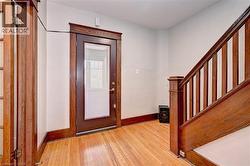Entryway featuring wood-finish flooring, a dark wood-finish front door with an integrated window pane, rich wood-finish trim, and a wood-finish staircase with balusters - 