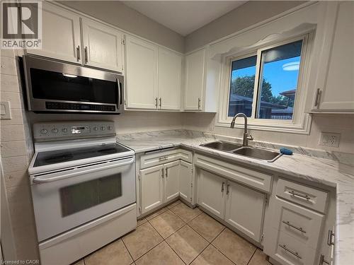 White cabinetry with brushed nickel hardware, stainless steel microwave, dual basin sink with brushed nickel faucet, light-toned countertops, and tiled flooring - 70 Eagen Drive Unit# Upper Level, Kitchener, ON - Indoor Photo Showing Kitchen With Double Sink
