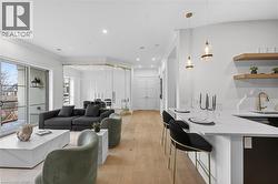 Light wood-finish flooring, recessed lighting, and a white countertop with a waterfall edge - 