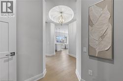 Recessed ceiling with an ornate light fixture, light wood-finish flooring, and white baseboard molding - 