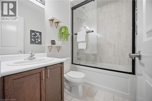 Bathroom featuring a shower-tub combination with glass enclosure, white tile surround, a wood-finish vanity with an integrated sink, and light-toned floor tile - 20 Todd Crescent, Dundalk, ON - Indoor Photo Showing Bathroom