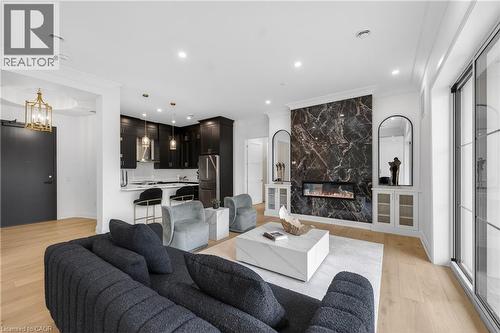 Open-concept living area with light wood-finish flooring, a contemporary fireplace featuring a dark stone-look surround, and built-in cabinetry - 2 Arbourvale Common Unit# 209, St. Catharines, ON - Indoor Photo Showing Living Room With Fireplace