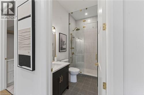 Bathroom featuring a dark wood vanity with white countertop, circular mosaic floor tiles, a frameless glass shower enclosure, and brass fixtures - 2 Arbourvale Common Unit# 209, St. Catharines, ON - Indoor Photo Showing Bathroom