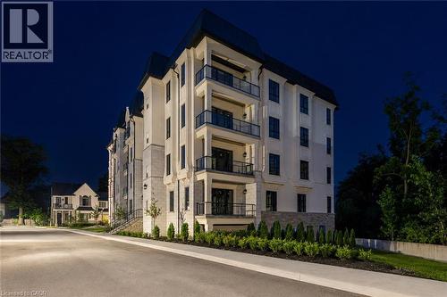Multi-story building featuring a stone and stucco facade, individual balconies with glass railings, and a sloped roofline - 2 Arbourvale Common Unit# 209, St. Catharines, ON - Outdoor With Balcony With Facade