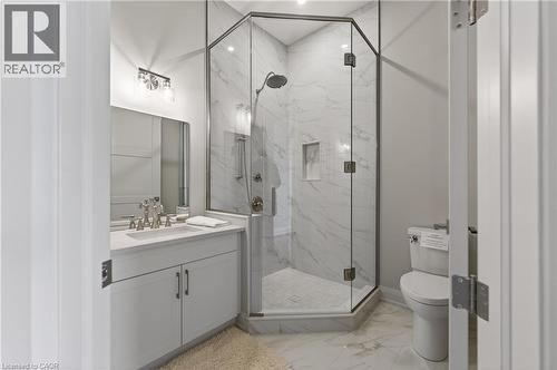 Bathroom featuring a vanity with an integrated sink, a glass-enclosed shower, a built-in shower niche, and wall-mounted light fixtures - 2 Arbourvale Common Unit# 209, St. Catharines, ON - Indoor Photo Showing Bathroom