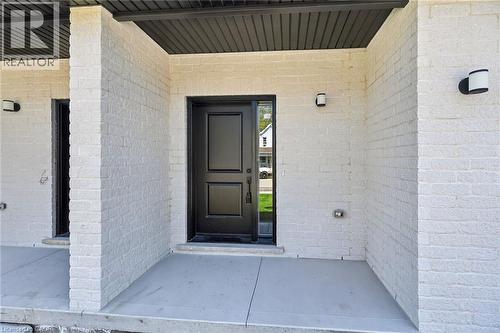 Contemporary entry featuring a black paneled door with sidelight, white painted brick facade, concrete porch, and black outdoor sconces - 45B Howard Street, Hagersville, ON 