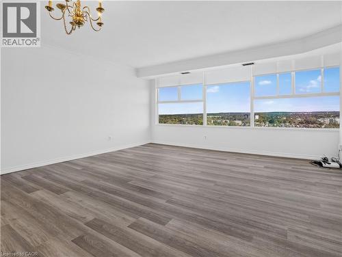 Spacious room featuring wood-finish flooring, extensive window line, and a decorative chandelier - 7 Gale Crescent Unit# 1107, St. Catharines, ON 