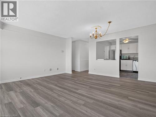 Wood-finish flooring throughout, crown molding detail, recessed wall cut-out, and a kitchen featuring white cabinetry and appliances - 7 Gale Crescent Unit# 1107, St. Catharines, ON 