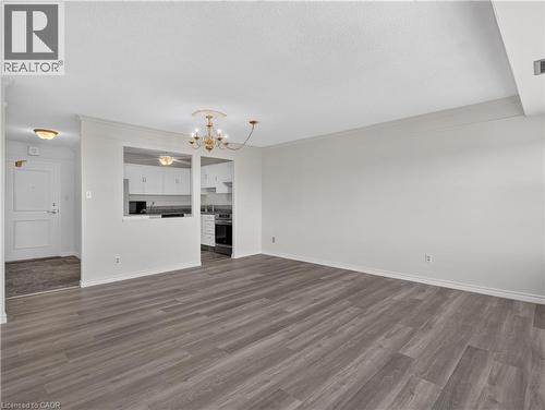 Spacious living area featuring wood-finish flooring, a decorative chandelier, and an open pass-through to the kitchen with white cabinetry - 7 Gale Crescent Unit# 1107, St. Catharines, ON 