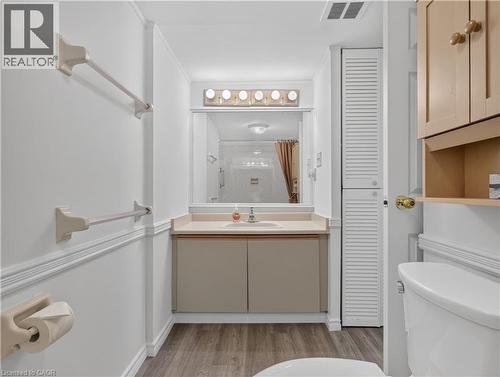 Vanity with an integrated sink and base cabinetry, complemented by a large mirror and overhead lighting - 7 Gale Crescent Unit# 1107, St. Catharines, ON 