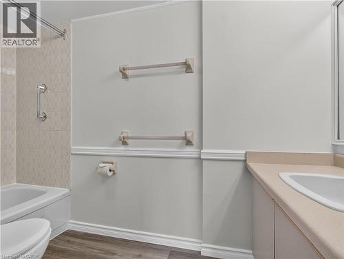 Integrated bathtub with a tiled shower surround, wall-mounted grab bar, wood-finish flooring, white vanity with a rectangular basin, and a light-toned countertop - 7 Gale Crescent Unit# 1107, St. Catharines, ON 