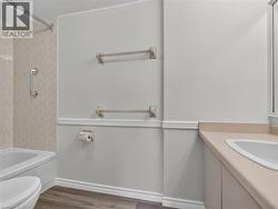 Integrated bathtub with a tiled shower surround, wall-mounted grab bar, wood-finish flooring, white vanity with a rectangular basin, and a light-toned countertop - 