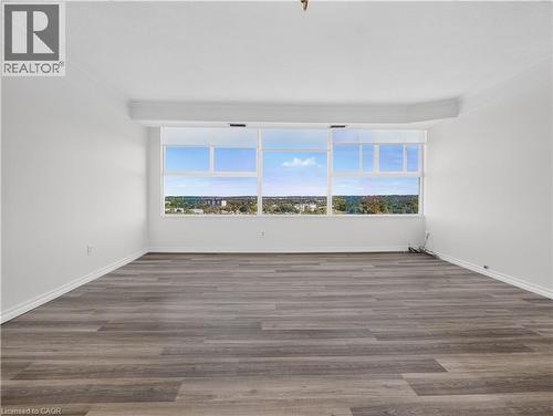 Expansive room featuring wood-finish flooring, white painted walls, crown molding, and large window banks - 7 Gale Crescent Unit# 1107, St. Catharines, ON 