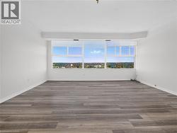 Expansive room featuring wood-finish flooring, white painted walls, crown molding, and large window banks - 