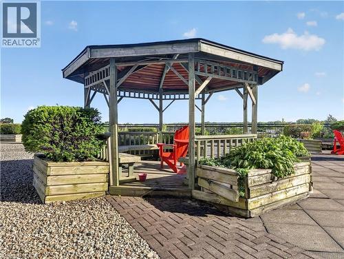 Wooden gazebo with built-in bench seating, surrounded by planter boxes, on a paved surface - 7 Gale Crescent Unit# 1107, St. Catharines, ON 