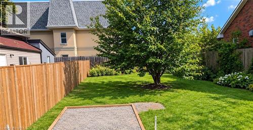 Expansive grassy lawn with a mature tree, bordered by wood fencing and a gravel-filled recreation area - 106 Catharine Avenue, Brantford, ON 