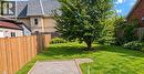 Expansive grassy lawn with a mature tree, bordered by wood fencing and a gravel-filled recreation area - 106 Catharine Avenue, Brantford, ON 