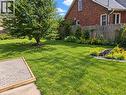 Expansive green lawn featuring a mature shade tree, a gravel patio area, and a brick house exterior - 106 Catharine Avenue, Brantford, ON 