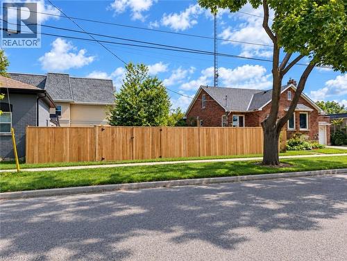 Brick exterior with a dark shingle roof, mature front yard tree, and a newly installed wood privacy fence - 106 Catharine Avenue, Brantford, ON 