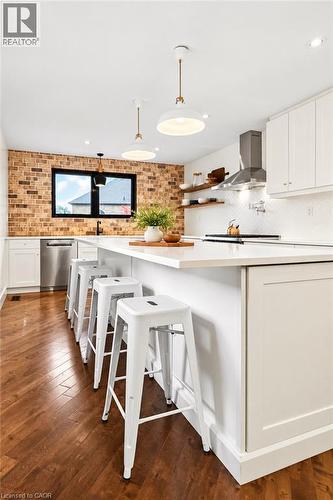 Kitchen featuring wood-finish flooring, brick-accent wall, white shaker cabinetry, stainless steel appliances, and a central island with countertop - 9 Midway Street, Hamilton, ON 
