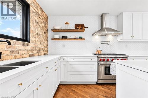 White cabinetry with gold-tone hardware, white countertops, stainless steel range with matching vent hood, and a chevron-patterned tile backsplash - 9 Midway Street, Hamilton, ON 